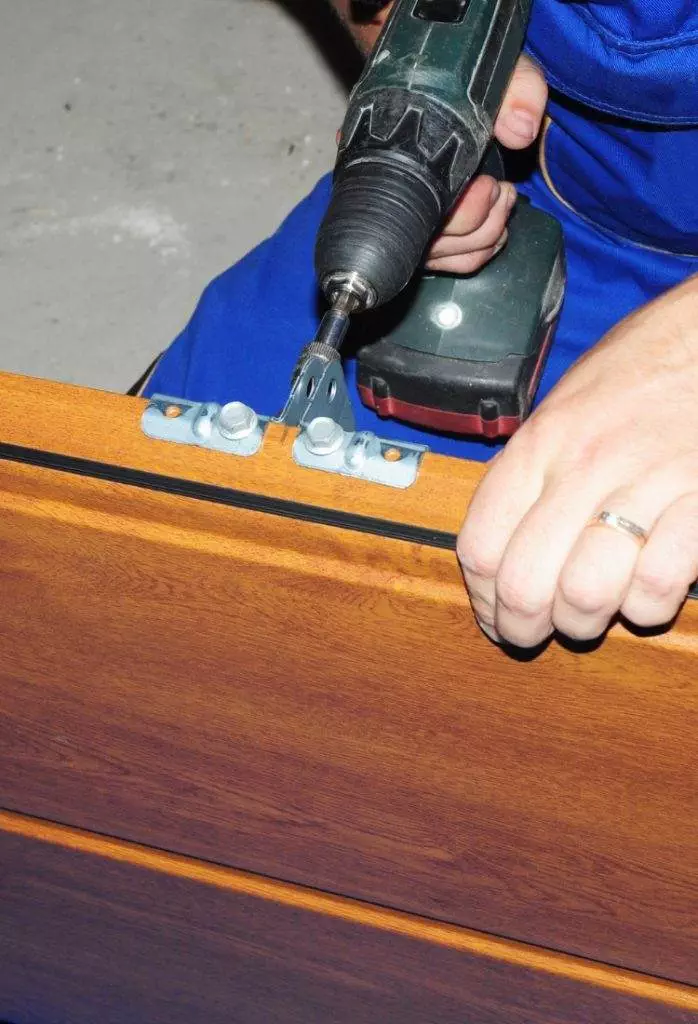 Expert craftsman installs cabinet hinge with electric drill in workshop at daytime