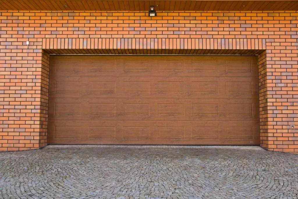 A peaceful suburban driveway leading to a closed garage surrounded by lush greenery in early fall