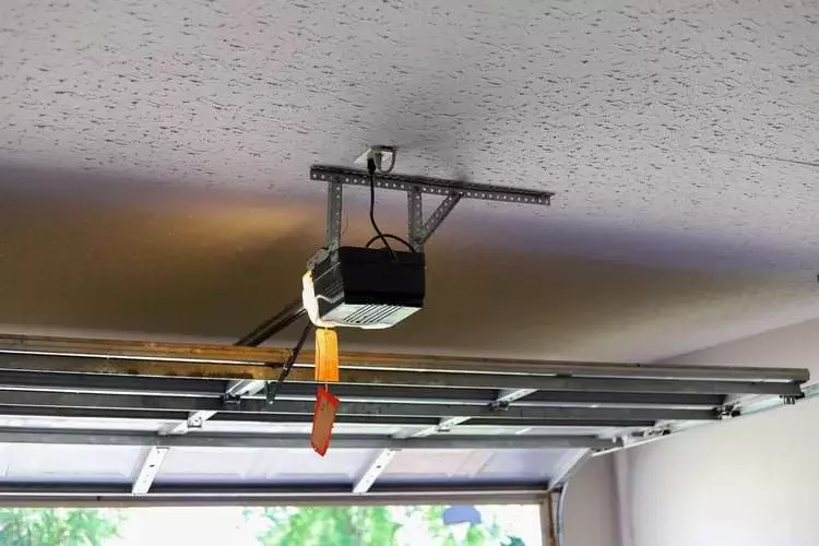 Garage door opener installed on the ceiling with a view of the partially open door