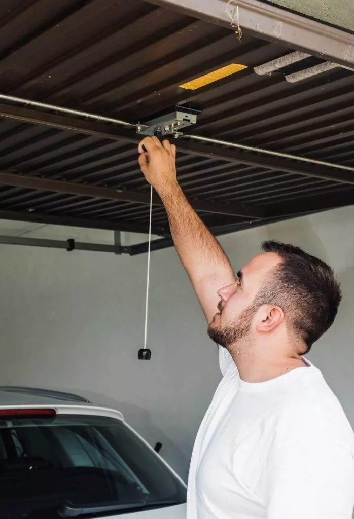 Man adjusting garage door opener in residential garage during daytime repair