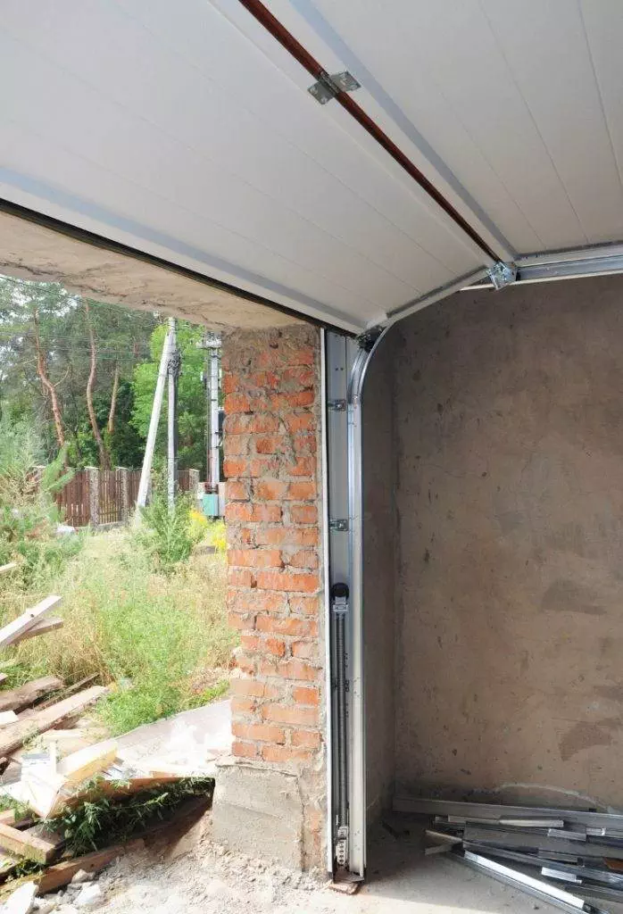 Construction of a garage interior with a partially opened door, tools, and unfinished walls