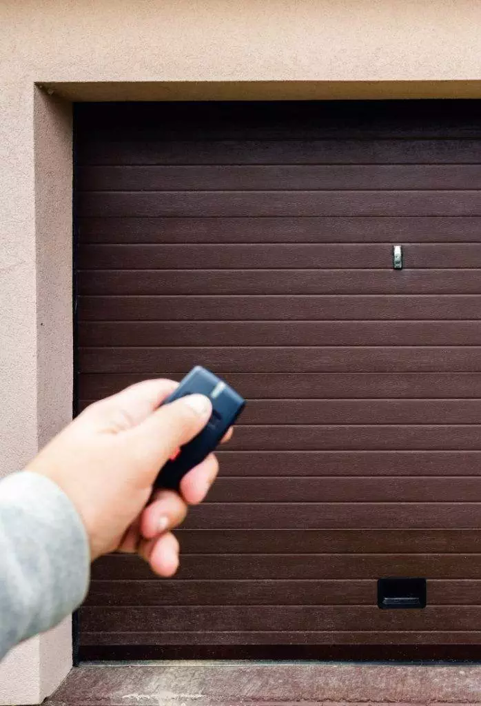 Hand holding garage door remote control outside home ready to open overhead door