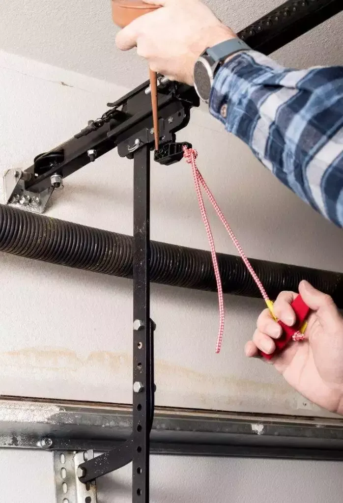 Person adjusting garage door mechanism with tape measure and tools in indoor space